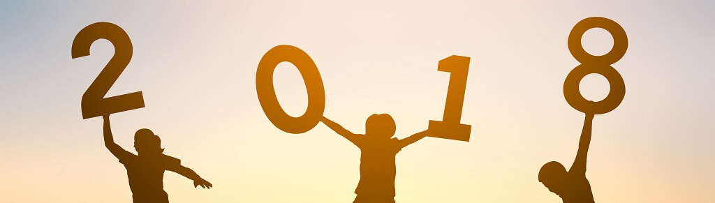 Silhouetted against a sunset sky, four children each hold up a large number to form "2018". They are positioned in a row, each child holding one number. The children are celebrating, with their arms raised high, marking the end of an unforgettable year in review.